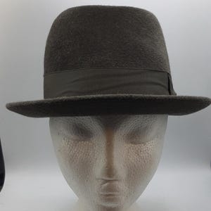 May include: A dark gray fedora hat with a grosgrain ribbon band. The hat has a rounded crown and a wide brim. This classic hat is a stylish accessory.