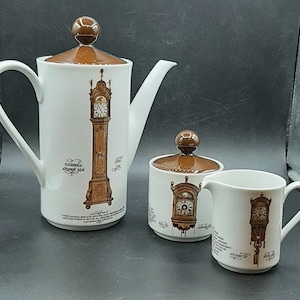 May include: A white porcelain tea set with a brown lid and brown accents. The set features a clock design with the text "Hollandse straalt klok" and "1792".