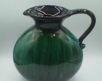 May include: A green ceramic pitcher with a black rim and handle. The pitcher has a round body and a slightly flared lip.