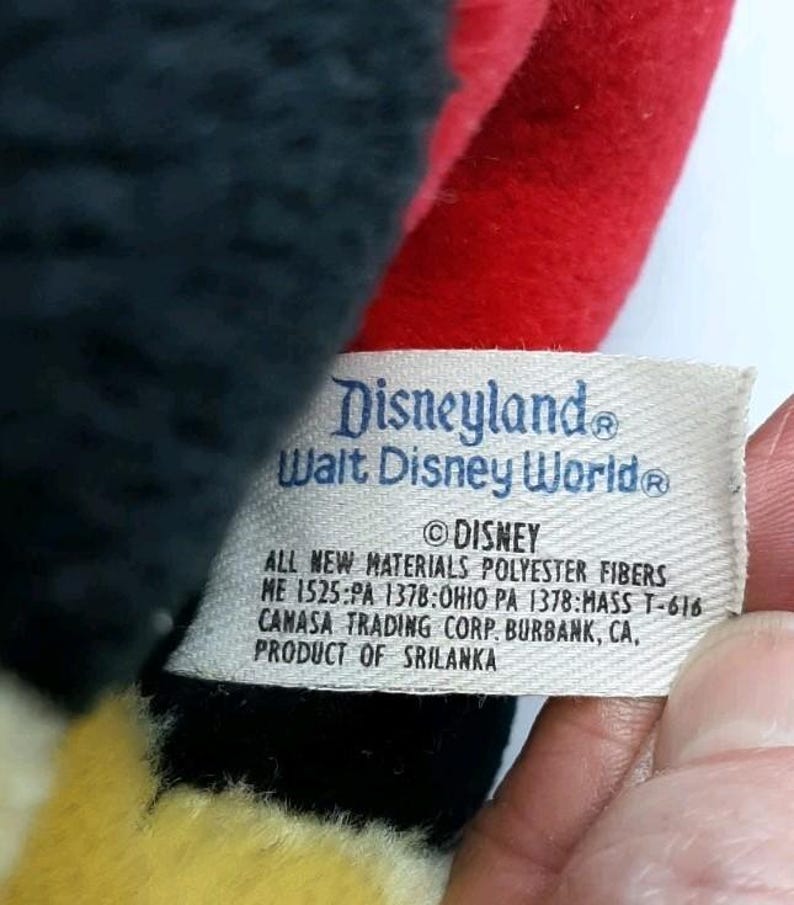 May include: Close-up of a vintage Disney plush toy. The tag reads "Disneyland Walt Disney World" and includes the Disney copyright. The toy is made of black, red, and yellow fabric.