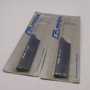 May include: Two dark blue combs in their original packaging. The packaging is gray and white with the brand name "Comair" in blue. The text "Blue Ribbon Stylers" and "Unconditionally Guaranteed" are also visible.