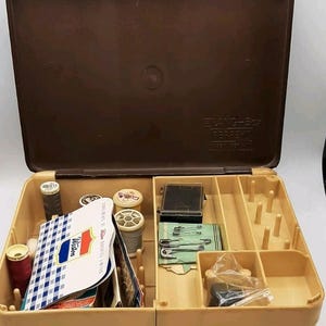 May include: Open sewing box with a brown lid and a tan base. The box contains spools of thread in various colors, needles, pins, and other sewing supplies. The box is labeled "ELANG-Box" and "Pepperell".