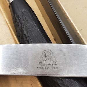 Puede incluir: Primer plano de un juego de cuchara y servidor de helado de acero inoxidable. Los mangos son negros con un dise&ntilde;o texturizado. El servidor tiene el texto "OLD FORGE STAINLESS STEEL".