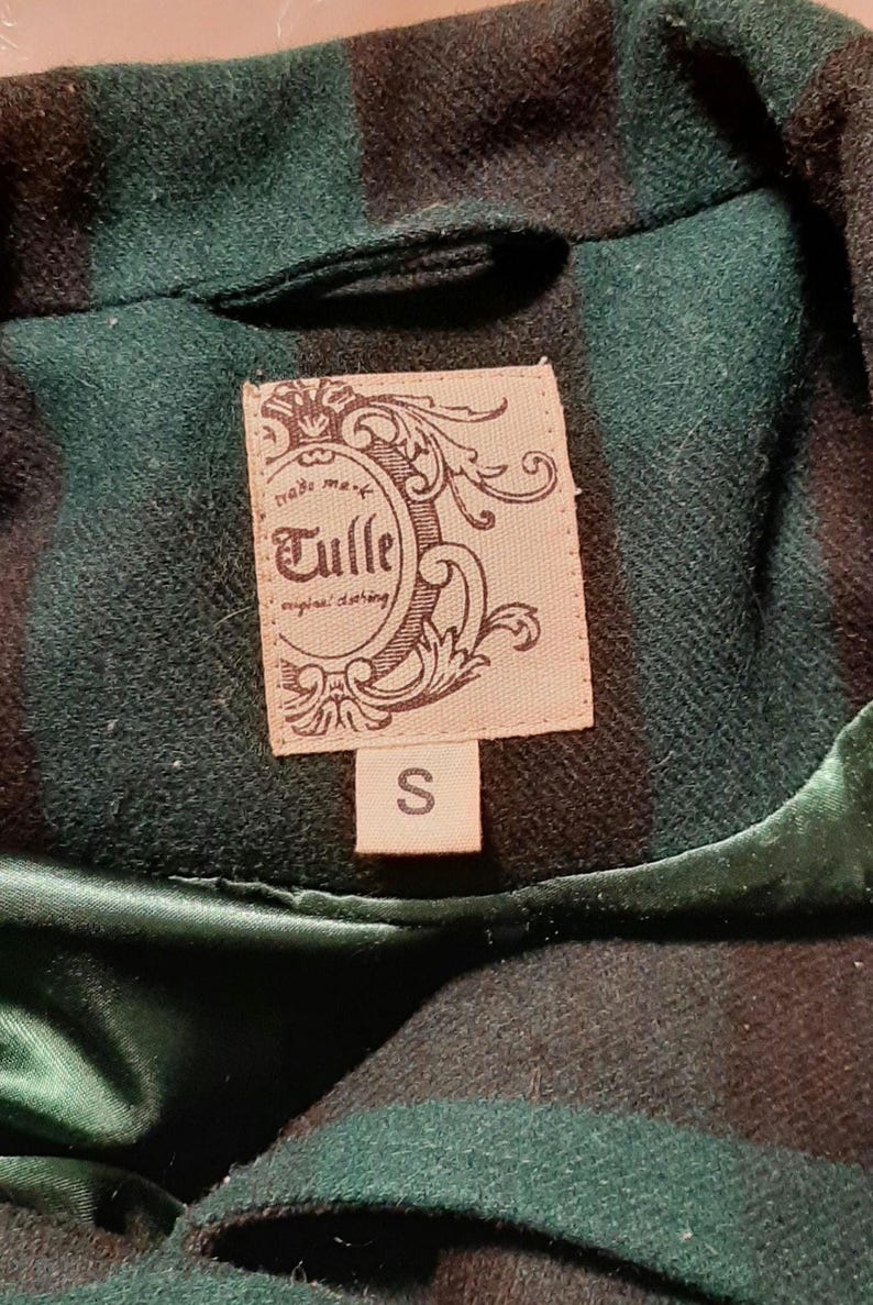 May include: A close-up of a green and black plaid jacket collar. The jacket has a satin lining and a label that reads "Tulle original clothing" with a size "S" label.