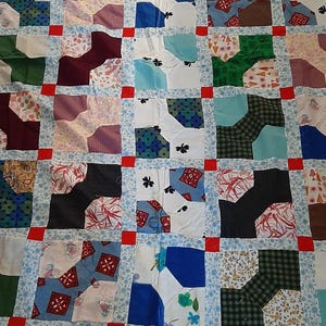 May include: A patchwork quilt featuring a range of colourful fabrics and patterns. The quilt is composed of squares and rectangles, with the fabric sewn together in a grid design. The quilt incorporates a mix of blues, greens, reds, and pinks.