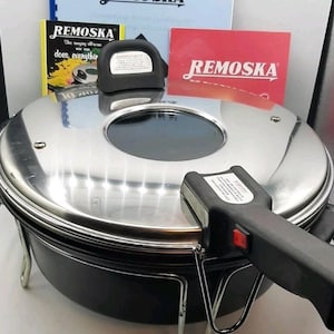 May include: A Remoska electric cooker in silver and black, featuring a glass viewing window. It has a black handle and is shown with instruction manuals and a red card, all branded with the Remoska logo. Designed for cooking.