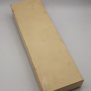 Puede incluir: Una caja rectangular beige con una superficie texturizada. La caja est&aacute; ligeramente desgastada, con algo de decoloraci&oacute;n y peque&ntilde;os da&ntilde;os en los bordes. La caja est&aacute; vac&iacute;a.