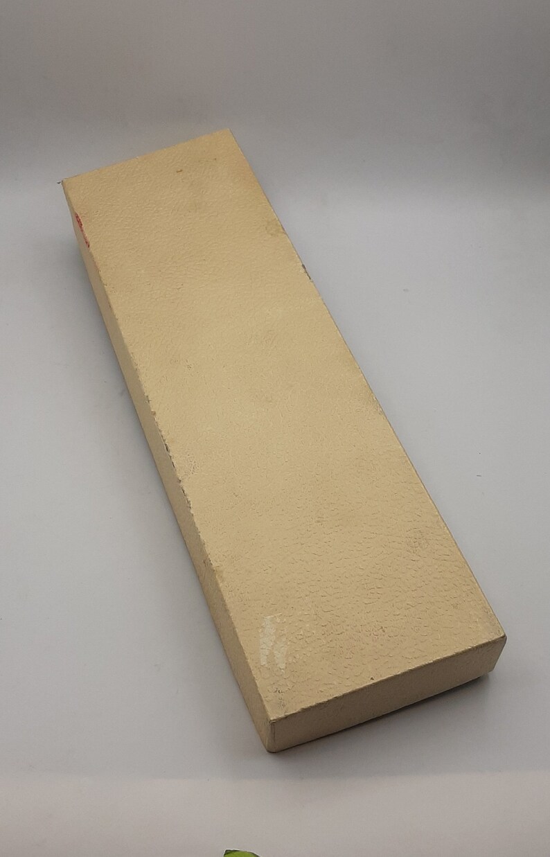 Puede incluir: Una caja rectangular beige con una superficie texturizada. La caja est&aacute; ligeramente desgastada, con algo de decoloraci&oacute;n y peque&ntilde;os da&ntilde;os en los bordes. La caja est&aacute; vac&iacute;a.