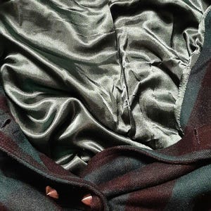 May include: Close-up of a dark green and burgundy plaid coat with a satin lining. The coat has a label that reads "Tulle" and the size "S". The coat is buttoned with two metal studs.