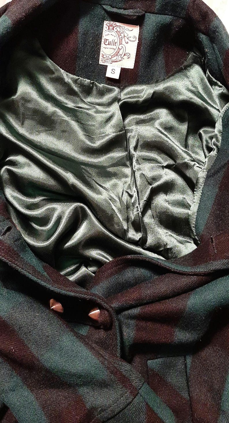 May include: Close-up of a dark green and burgundy plaid coat with a satin lining. The coat has a label that reads "Tulle" and the size "S". The coat is buttoned with two metal studs.