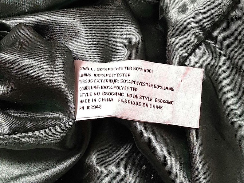 May include: A close-up of a garment's interior, displaying a label with fabric composition details. The label states "SHELL: 50% POLYESTER 50% WOOL" and "LINING: 100% POLYESTER." The garment is made in China.