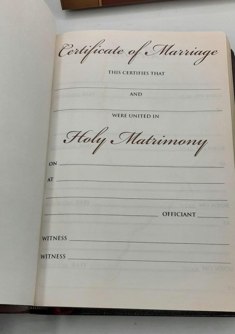 May include: Open book with a Certificate of Marriage page. The text reads "Certificate of Marriage", "Holy Matrimony", and includes lines for names, dates, and witnesses. The page is cream-colored with brown text.