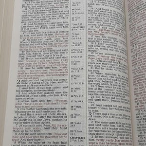 May include: Open Bible with text from the Gospel of John, featuring chapter and verse notations. The pages are yellowed, and the text is in black. The book is open to a specific passage.