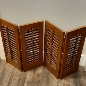 Puede incluir: Cuatro contraventanas de madera con un acabado marrón cálido. Cada contraventana tiene lamas horizontales y un marco rectangular. Las contraventanas están dispuestas en zigzag, lo que sugiere que podrían usarse como separador de ambientes o elemento decorativo.