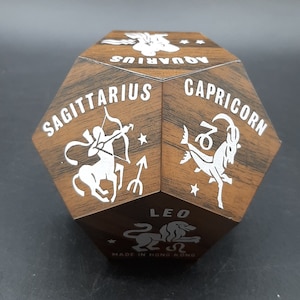 May include: A wooden, hexagonal box with a different zodiac sign on each side. The signs are Sagittarius, Capricorn, Leo, Aquarius, Pisces, and Virgo. The box is made in Hong Kong.
