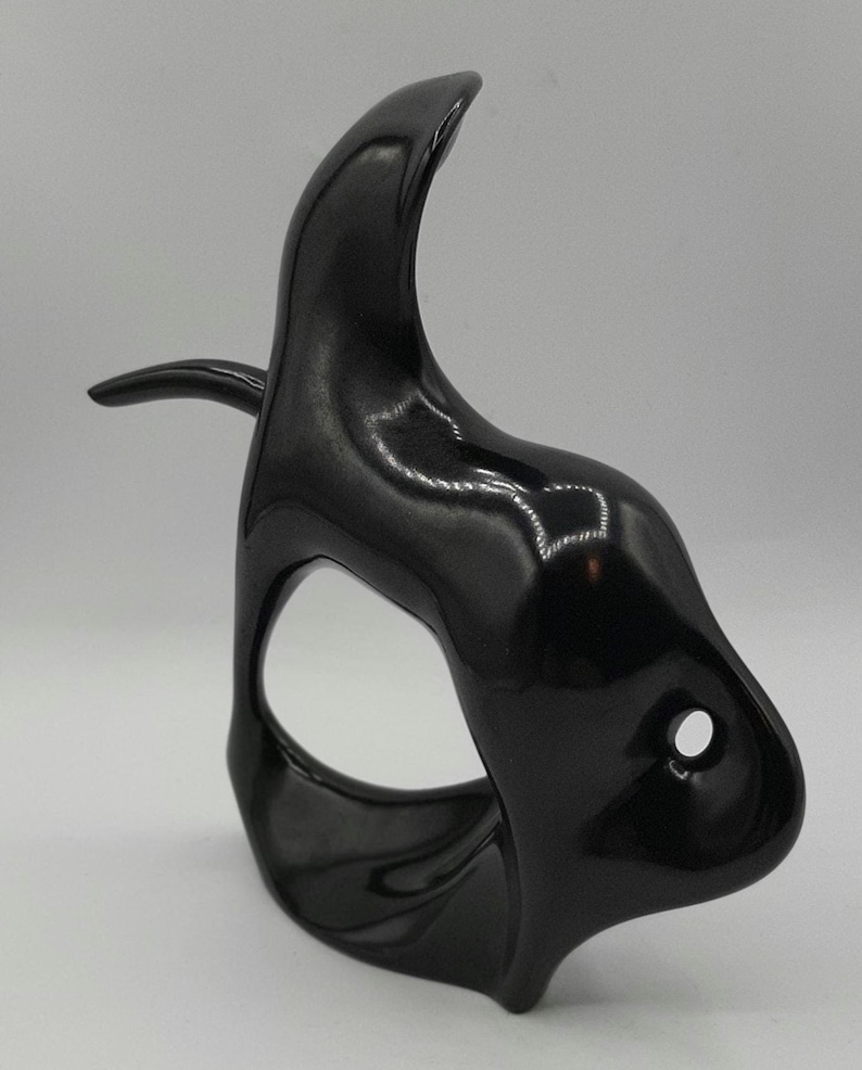 May include: A glossy black decorative mask with a curved, horn-like top and a small, protruding side element. The mask has a large, oval-shaped eye opening and a small, circular hole near the bottom.