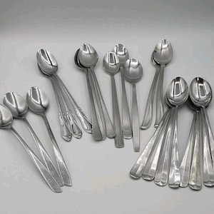 May include: A selection of stainless steel spoons in various styles. The spoons are displayed on a white surface, with different handle designs and bowl shapes visible. Some spoons have decorative handles, while others have a more minimalist design.