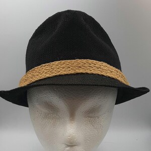 May include: A black fedora hat with a tan woven band. The hat has a classic design with a slightly curved brim. The hat is displayed on a white mannequin head.