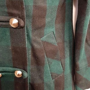 May include: Green and brown plaid coat with gold-coloured buttons. The coat has a tailored fit, a pocket, and a classic design. The fabric appears to be a wool blend, suitable for colder weather. The buttons are large and decorative.