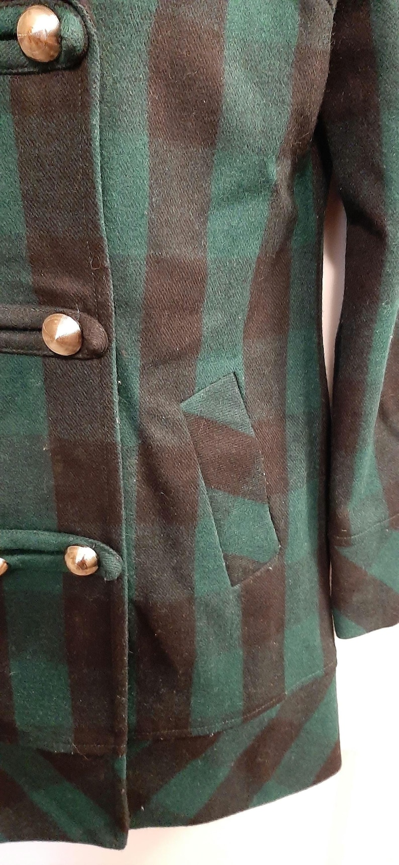 May include: Green and brown plaid coat with gold-coloured buttons. The coat has a tailored fit, a pocket, and a classic design. The fabric appears to be a wool blend, suitable for colder weather. The buttons are large and decorative.