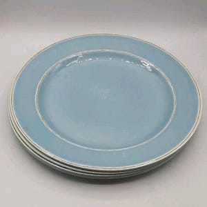 Peut inclure: Une pile de trois assiettes rondes en céramique de couleur bleu clair uni. Chaque assiette présente une finition lisse et brillante avec un bord légèrement surélevé et un fin détail de bordure blanc cassé le long de la circonférence.