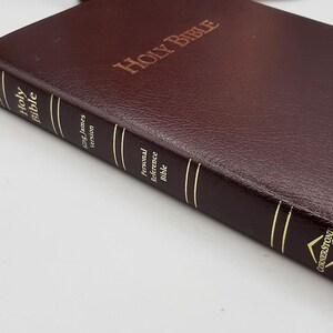 May include: A burgundy leather-bound Holy Bible with gold-gilded page edges. The cover is embossed with "Holy Bible" in gold lettering. The spine features the text "Holy Bible", "King James Version", and "Personal Reference Bible".