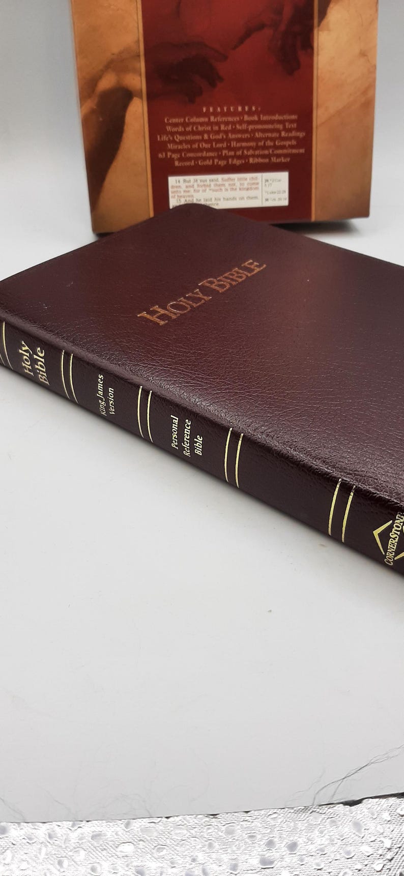 May include: A burgundy leather-bound Holy Bible with gold-gilded page edges. The cover is embossed with "Holy Bible" in gold lettering. The spine features the text "Holy Bible", "King James Version", and "Personal Reference Bible".