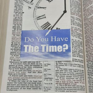 May include: A page from a Bible with text and a clock overlay reading "Do You Have The Time?". The clock face is white with black Roman numerals and hands. The text is in English.