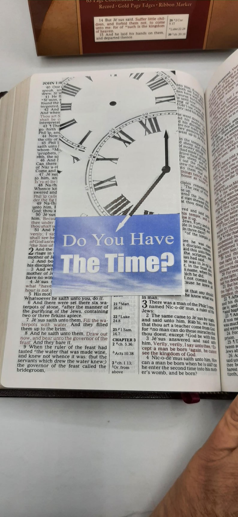 May include: A page from a Bible with text and a clock overlay reading "Do You Have The Time?". The clock face is white with black Roman numerals and hands. The text is in English.