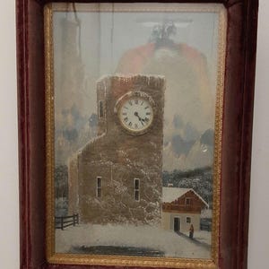 May include: A framed painting of a snowy winter scene with a clock tower in the center. The clock tower is made of stone and has a clock face with Roman numerals. The painting is set in a dark red velvet frame with a gold trim.