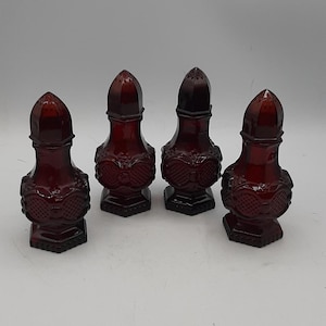 Op de afbeelding: Vier antieke zout- en peperstrooiers van robijnrood glas. Elke strooier heeft een decoratief patroon en een conische bovenkant met kleine gaatjes. De strooiers hebben een zeshoekige basis en een bolvormig lichaam.