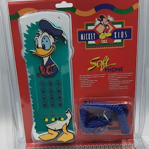 May include: A vintage Mickey Kids Soft Phone in its original packaging. The phone has a teal body with a Donald Duck design. The packaging includes the text "It's a REAL PHONE" and a coiled blue handset.