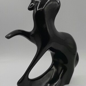 May include: A glossy black abstract sculpture with a flowing, organic form. The sculpture features a curved shape with an open center and an extended arm-like element. The artwork has a smooth, reflective surface.