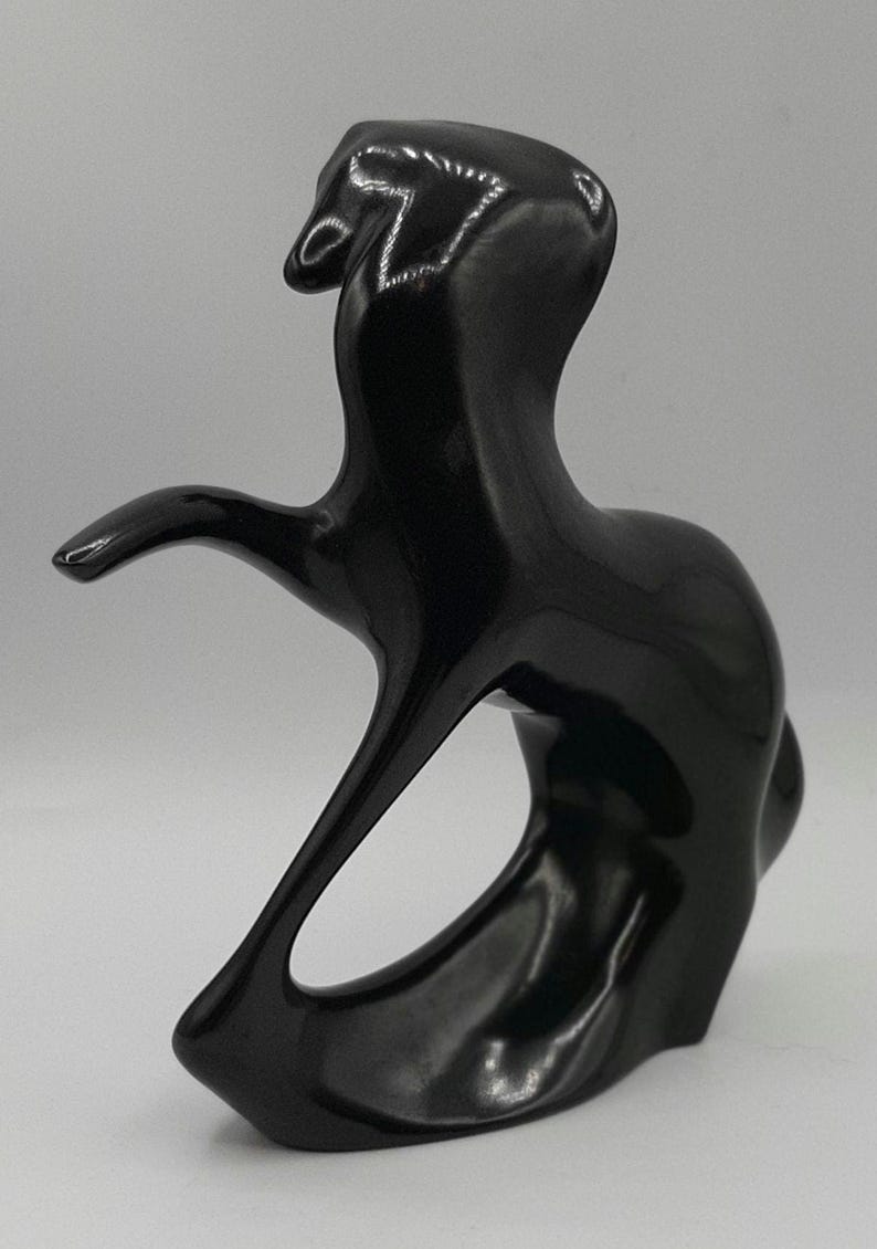 May include: A glossy black abstract sculpture with a flowing, organic form. The sculpture features a curved shape with an open center and an extended arm-like element. The artwork has a smooth, reflective surface.