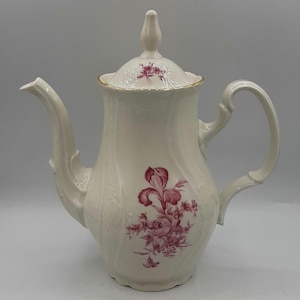 May include: A white porcelain coffee pot with a pink floral design and gold trim. The pot has a lid with a knob on top.