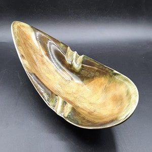 May include: A brown and green ceramic ashtray shaped like a curved leaf. The ashtray has a smooth, glossy finish and a unique, abstract design.