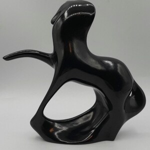 May include: A glossy black abstract sculpture with a smooth, curved form. The sculpture features an open, oval-shaped space in the center and an extended arm-like element. The overall design is modern and artistic.