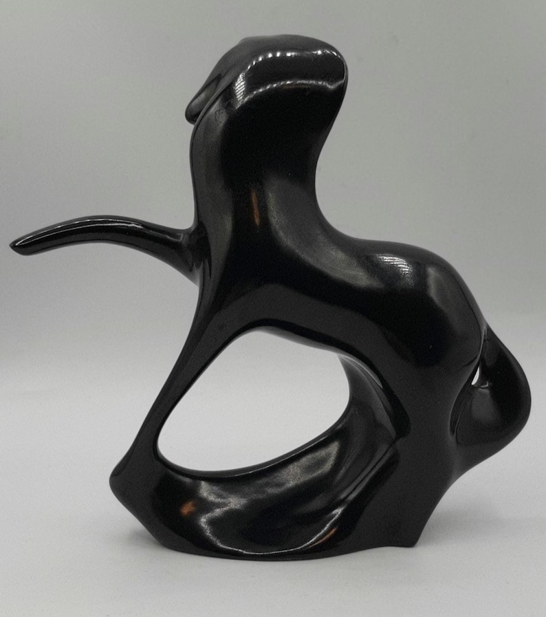 May include: A glossy black abstract sculpture with a smooth, curved form. The sculpture features an open, oval-shaped space in the center and an extended arm-like element. The overall design is modern and artistic.