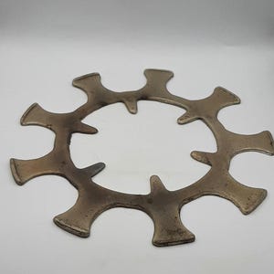 May include: A silver-colored metal ring with 12 points, resembling a gear or a starburst. The ring is circular and has a smooth, slightly worn surface.
