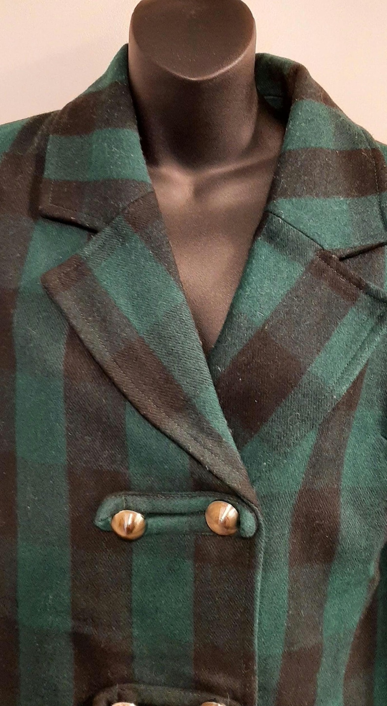 May include: Green and black checked blazer with gold buttons. The double-breasted jacket features a traditional notched lapel and a fitted silhouette. The material looks like a wool mix, ideal for colder climates. A vintage-style piece of clothing.