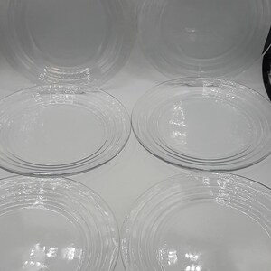 May include: Six clear glass dinner plates with a textured, concentric circle design.