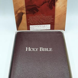 May include: A brown leather-bound Holy Bible with gold lettering, displayed in a white box. The cover reads "HOLY BIBLE" in gold. The box behind it displays "PERSONAL REFERENCE BIBLE" and "HOLY BIBLE".