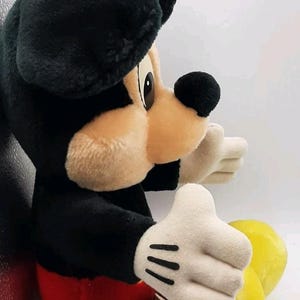 May include: A plush Mickey Mouse toy, featuring a black body, ears, and nose, with a tan face and white gloves. The toy has red shorts and yellow feet. A classic Disney character.