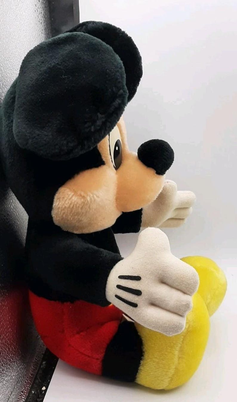 May include: A plush Mickey Mouse toy, featuring a black body, ears, and nose, with a tan face and white gloves. The toy has red shorts and yellow feet. A classic Disney character.