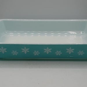 May include: Rectangular turquoise baking dish with white snowflake pattern around the sides. The interior is white, and the dish has handles on each end. A classic kitchenware item.