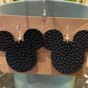 May include: A pair of black leather earrings shaped like Mickey Mouse ears. The earrings have silver hooks.