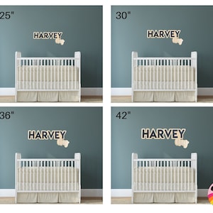 May include: Four images showcasing a white crib with a beige skirt, against a teal wall. Each image features a wooden sign that spells "HARVEY" and a small wooden shape. The signs are available in 25", 30", 36", and 42" sizes.