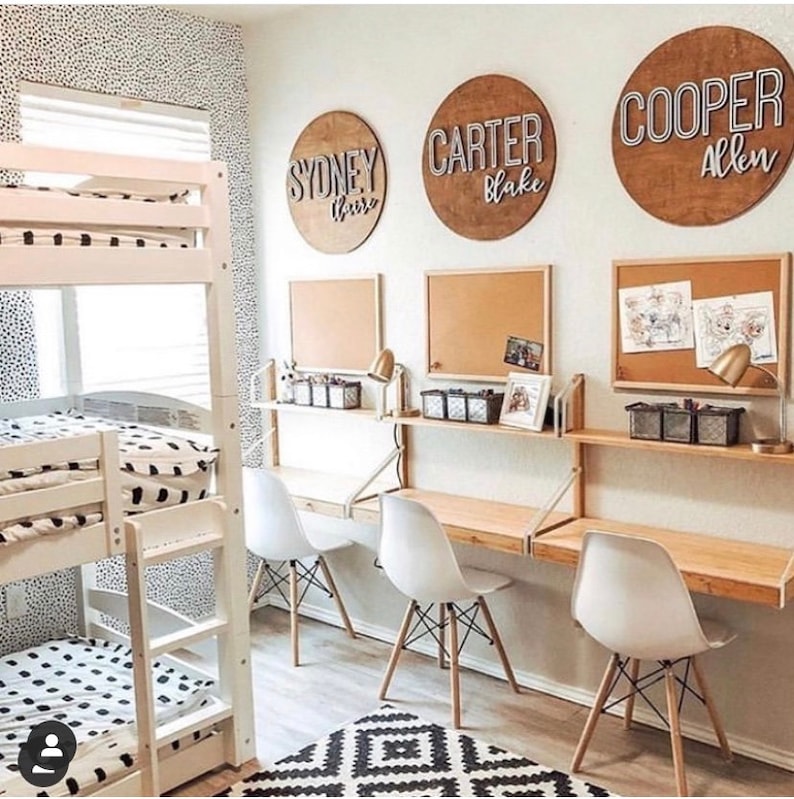 Puede incluir: Una litera blanca con ropa de cama con estampado blanco y negro. Tres sillas blancas con patas de madera est&aacute;n colocadas frente a un escritorio con una tapa de madera y soportes de metal blanco. Tres tableros de corcho con nombres escritos en ellos est&aacute;n en la pared detr&aacute;s del escritorio. Los nombres son "Sydney Blair", "Carter Blake" y "Cooper Allen".