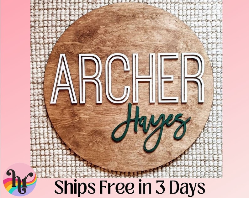 Puede incluir: Un letrero redondo de madera con el nombre "ARCHER Hayes" escrito en letras blancas y verdes. El nombre "ARCHER" est&aacute; en una fuente en negrita y en bloque con un contorno blanco. El nombre "Hayes" est&aacute; en una fuente cursiva con un contorno verde.