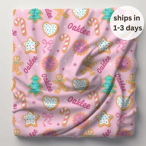 May include: Pink fabric with a repeating pattern of gingerbread cookies, candy canes, and Christmas trees. The fabric is personalized with the name "Oaklee".